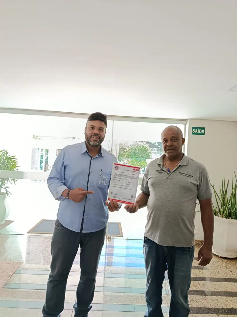 Técnico da FHS entregando o AVCB impresso ao responsável pelo condomínio no hall do edifício